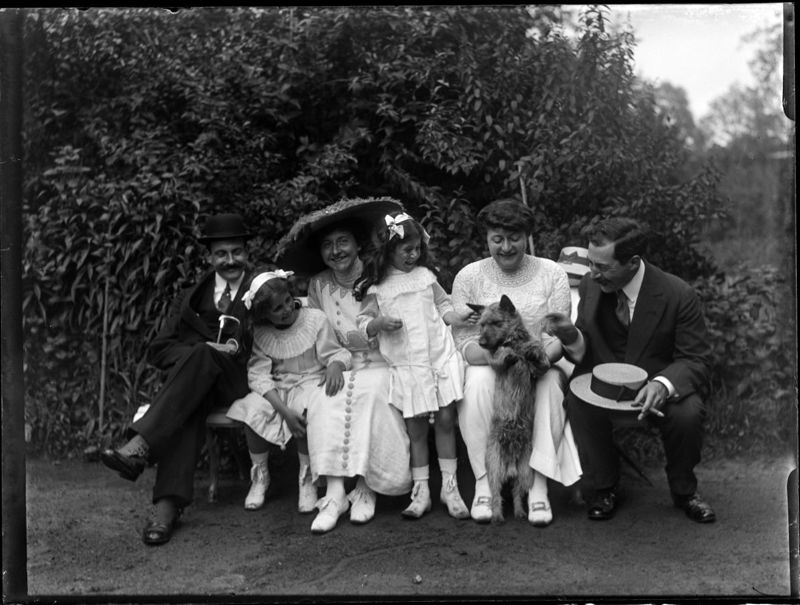 Portrait de groupe, six personnes assise sur un banc dans le jardin de Monsieur et Madame Emile Henri t'Serstevens