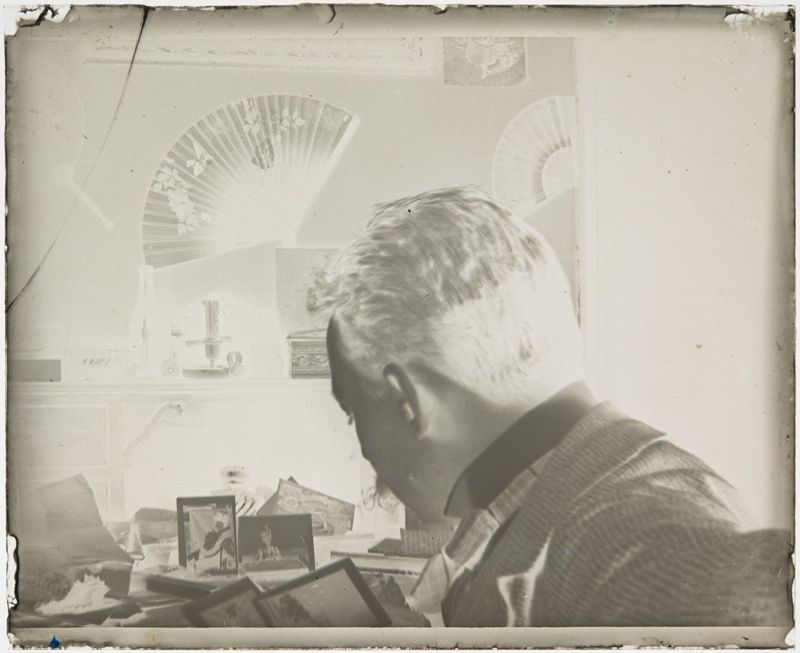 Henri Evenepoel assis devant une table de travail (de profil), regardant des photographies de Louise De Mey-van Mattenburgh, le Trieu-Colin, à Fooz-Wépion