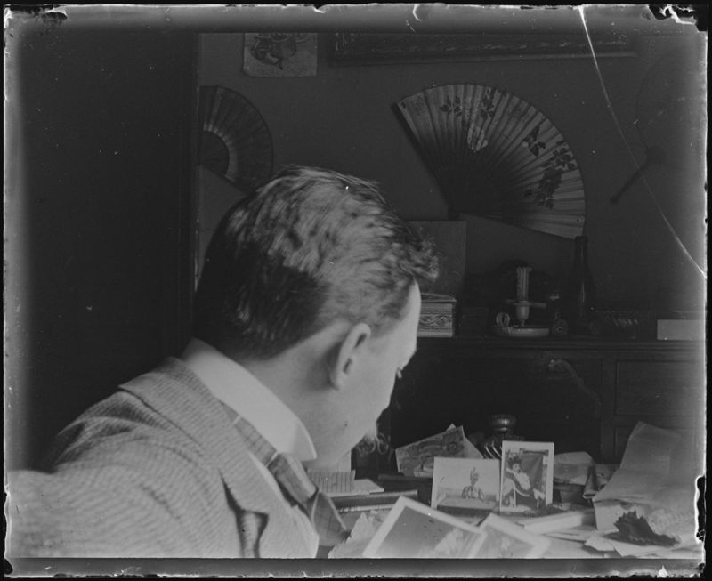 Henri Evenepoel assis devant une table de travail (de profil), regardant des photographies de Louise De Mey-van Mattenburgh, le Trieu-Colin, à Fooz-Wépion