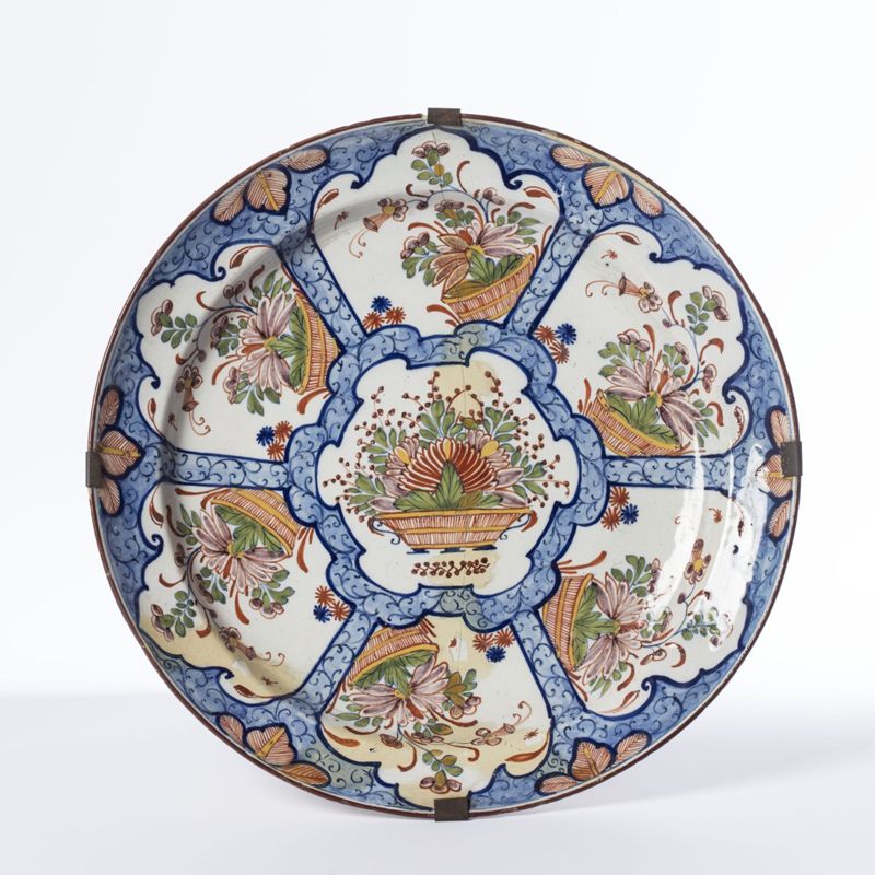 Plat en faïence de Delft au décor polychrome de sept paniers fleuris dans des réserves